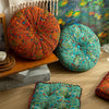 A vibrant, round bohemian cotton linen floor cushion in teal and green patterns rests on a wooden shelf.