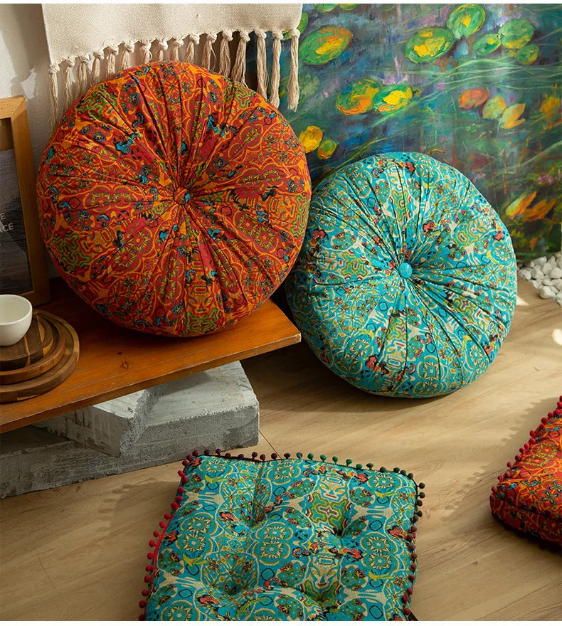 A vibrant, round bohemian cotton linen floor cushion in teal and green patterns rests on a wooden shelf.