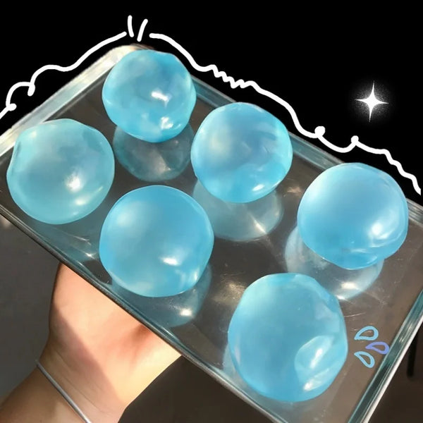 Une main tient un récipient transparent rempli de jouets anti-stress en mochi bleu clair et transparents.