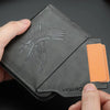Dunkelgraves Leder-Kartenwallet mit Vogel-Embossing und einer orangefarbenen Karte.