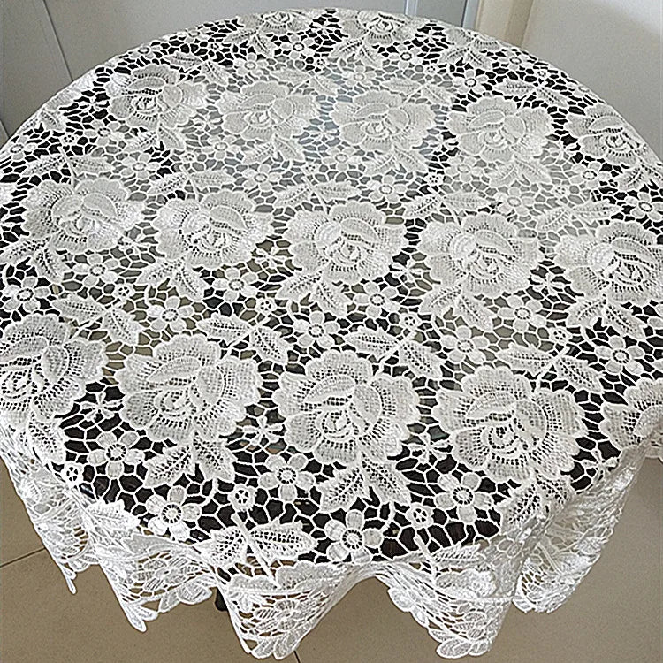 White lace tablecloth with embroidered rose pattern covering a round table.
