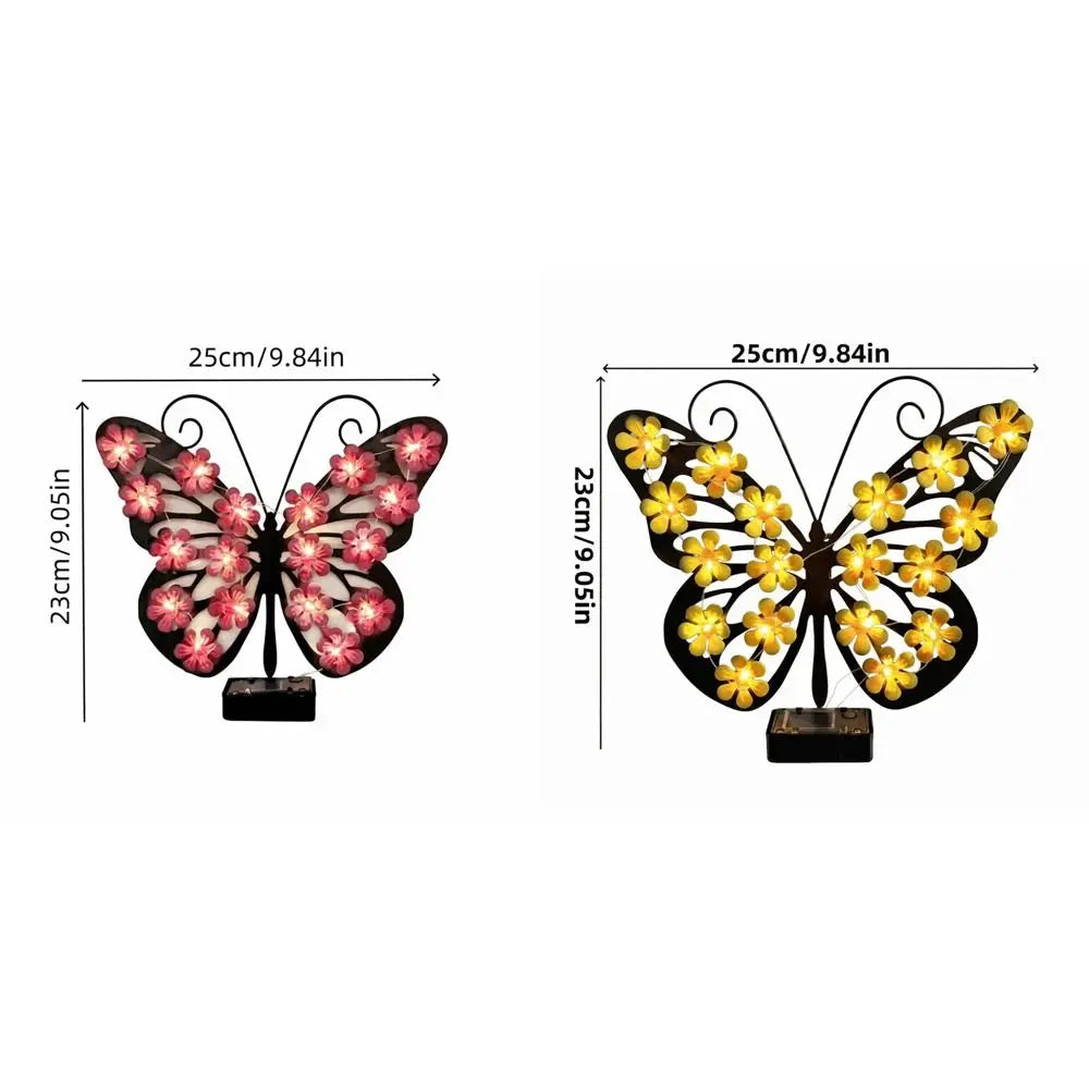 Applique murale à papillon solaire avec des ailes noires et des fleurs roses, montée sur une base sombre.