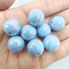 A hand holds several round, iridescent light blue acrylic beads for jewelry making.