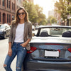 A young woman smiling while standing next to a dark gray car with a decorative rhinestone license plate frame.