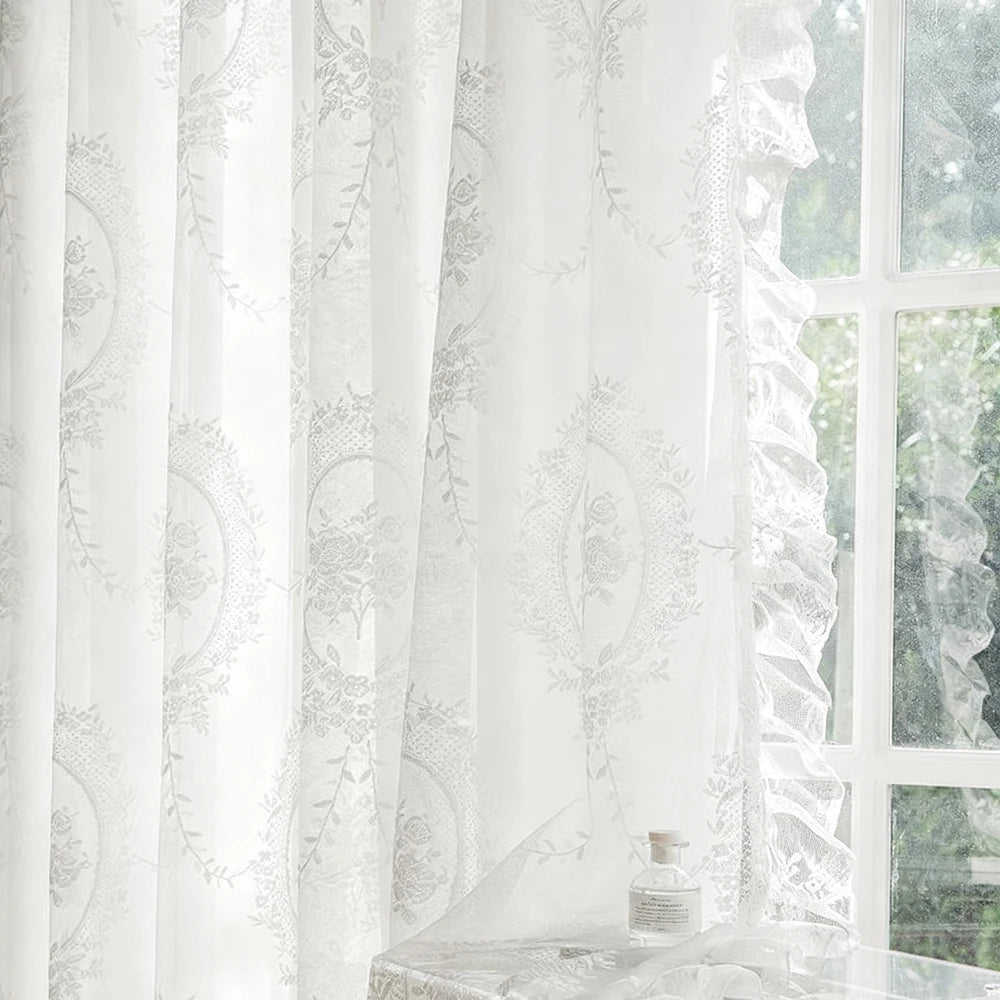 White sheer curtain with delicate lace embroidery filtering light through a window.