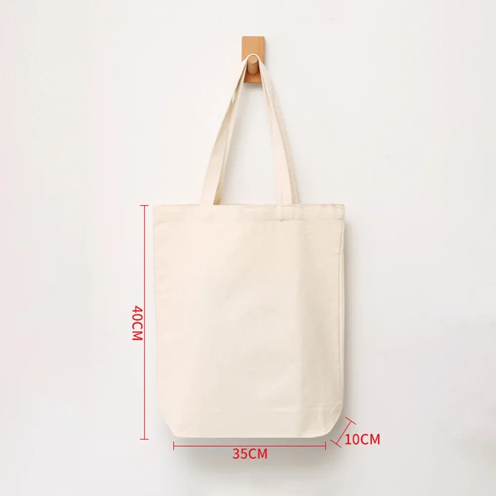 A plain off-white canvas shopping tote bag hanging from a wooden peg.