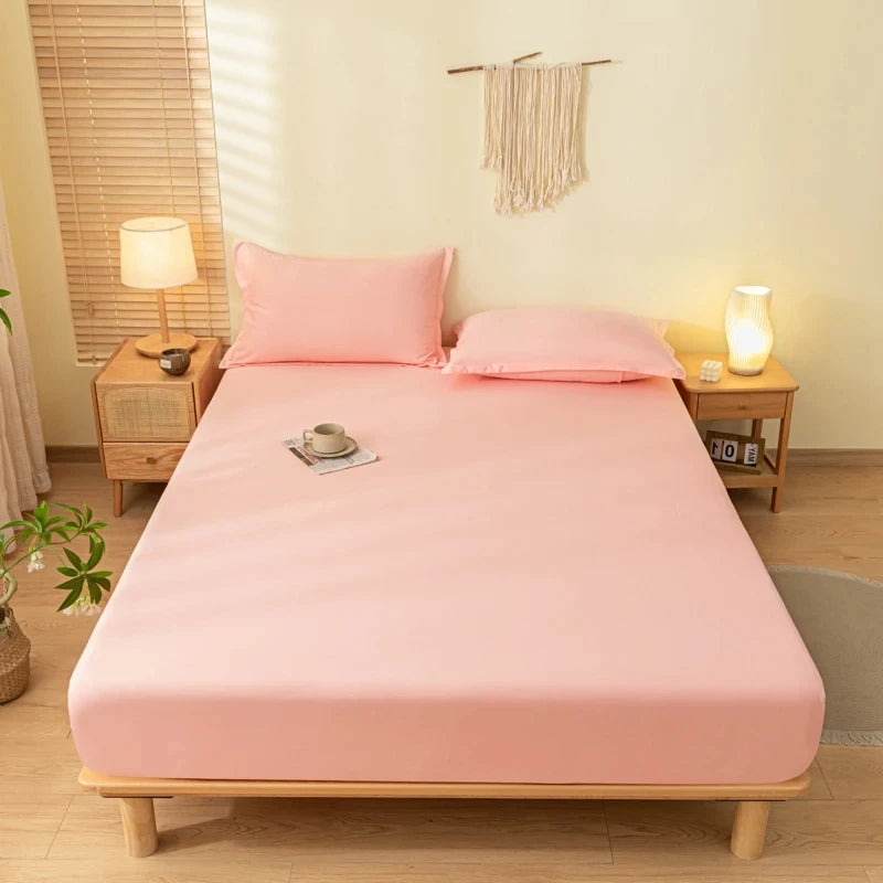 A pink fitted bed sheet set with pillows is displayed on a wooden bed frame in a bright room.