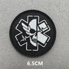 A round black patch featuring a white medical cross design with an eye motif.