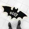 A black bat-shaped rug with white fluffy trim and the text 800! on it, placed on a white tiled floor.