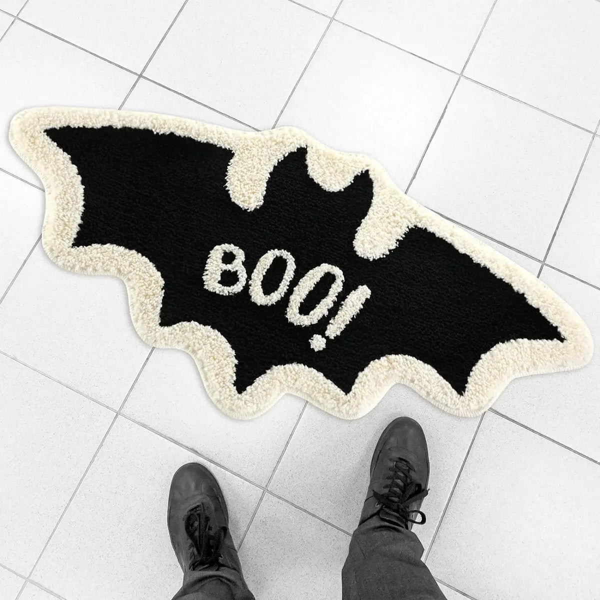 A black bat-shaped rug with white fluffy trim and the text 800! on it, placed on a white tiled floor.