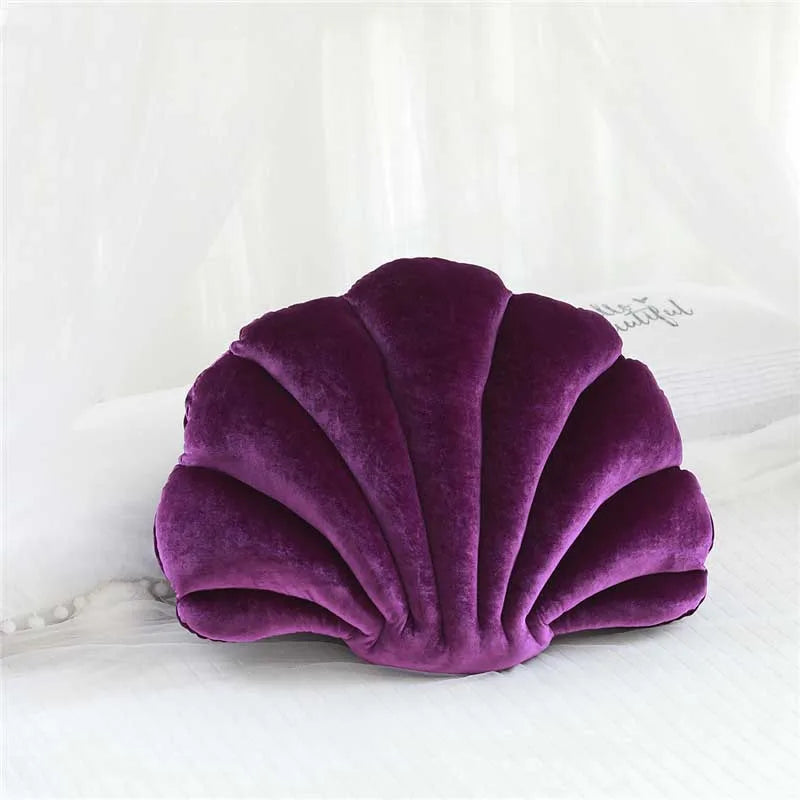 A deep purple velvet shell print throw pillow resting on white fabric.