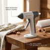 A white cordless hot glue gun with a gray nozzle guard sits on a wooden table, demonstrating an intelligent automatic shut-of