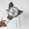 A hand holds a plush cover for a SEVENTEEN official light stick, featuring gray fur and a clear dome.