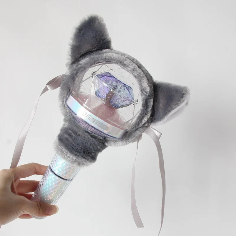 A hand holds a plush cover for a SEVENTEEN official light stick, featuring gray fur and a clear dome.
