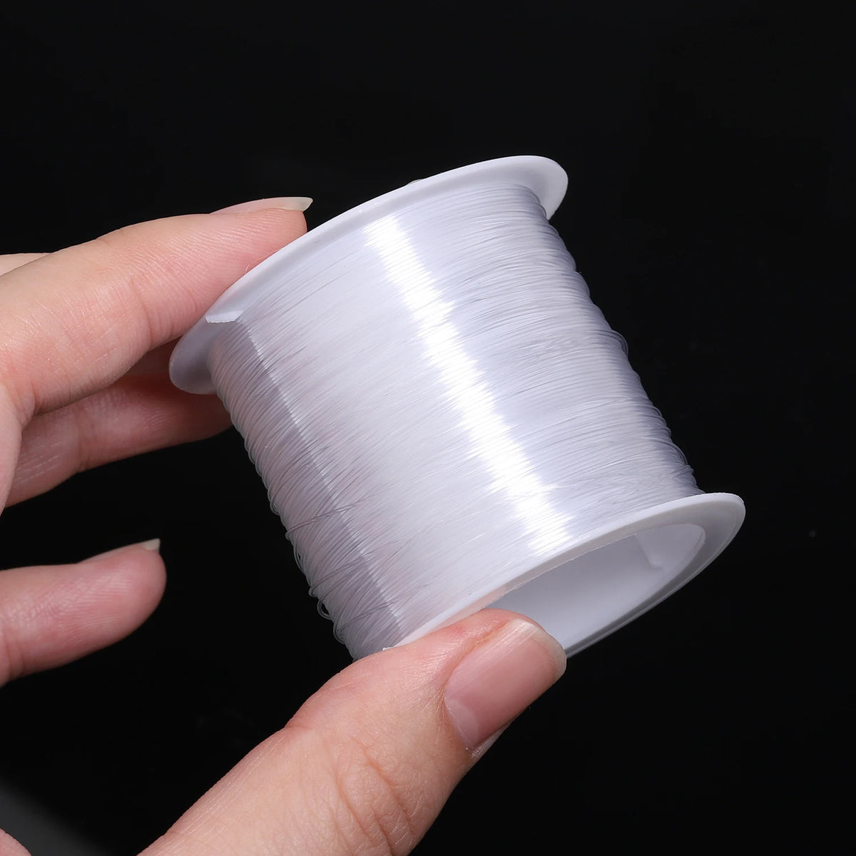 A hand holds a spool of white nylon beading cord for jewelry making.