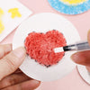 A hand applies red paint to a heart shape on white puffy texture painting paper for a DIY art project.