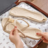 A hand is holding a beige foldable EVA travel slipper, showing the sole and strap design.