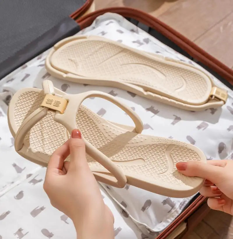 A hand is holding a beige foldable EVA travel slipper, showing the sole and strap design.