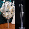 Clear plastic balloon column stands with gold confetti balloons displayed against a dark background.