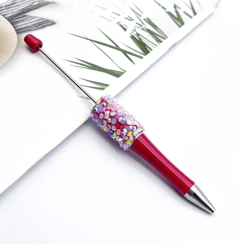 A close-up of a red ballpoint pen with a sparkly, multi-colored sequin tip resting on white paper.