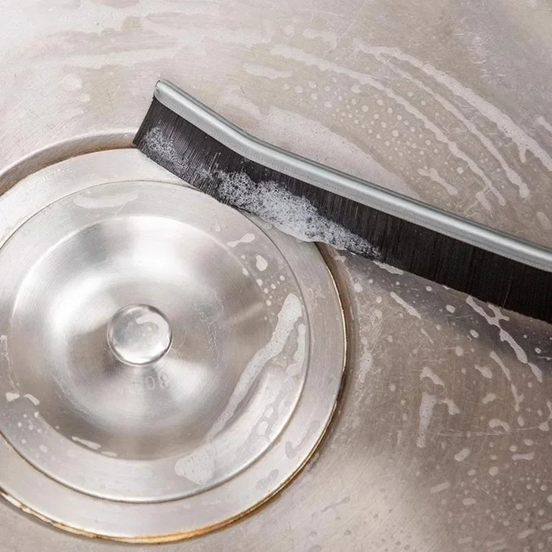 A close-up of a metal grout cleaning brush with black bristles resting on a circular metal cleaning disc.