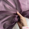 Close-up of mauve silk chiffon fabric being draped and folded by a hand.