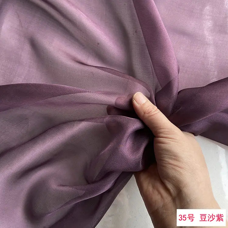 Close-up of mauve silk chiffon fabric being draped and folded by a hand.