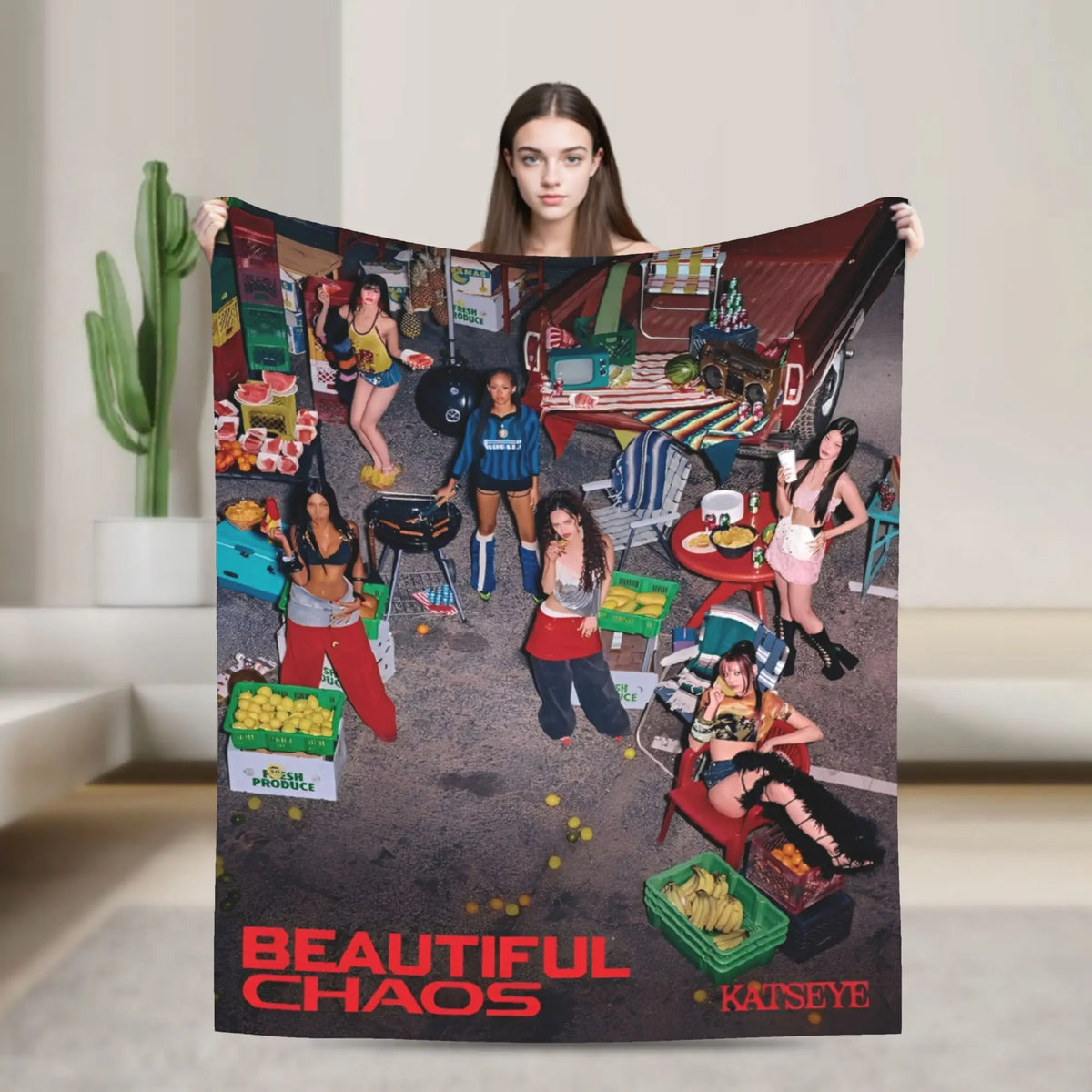 A person holds up a large throw blanket featuring a chaotic scene with people and objects.