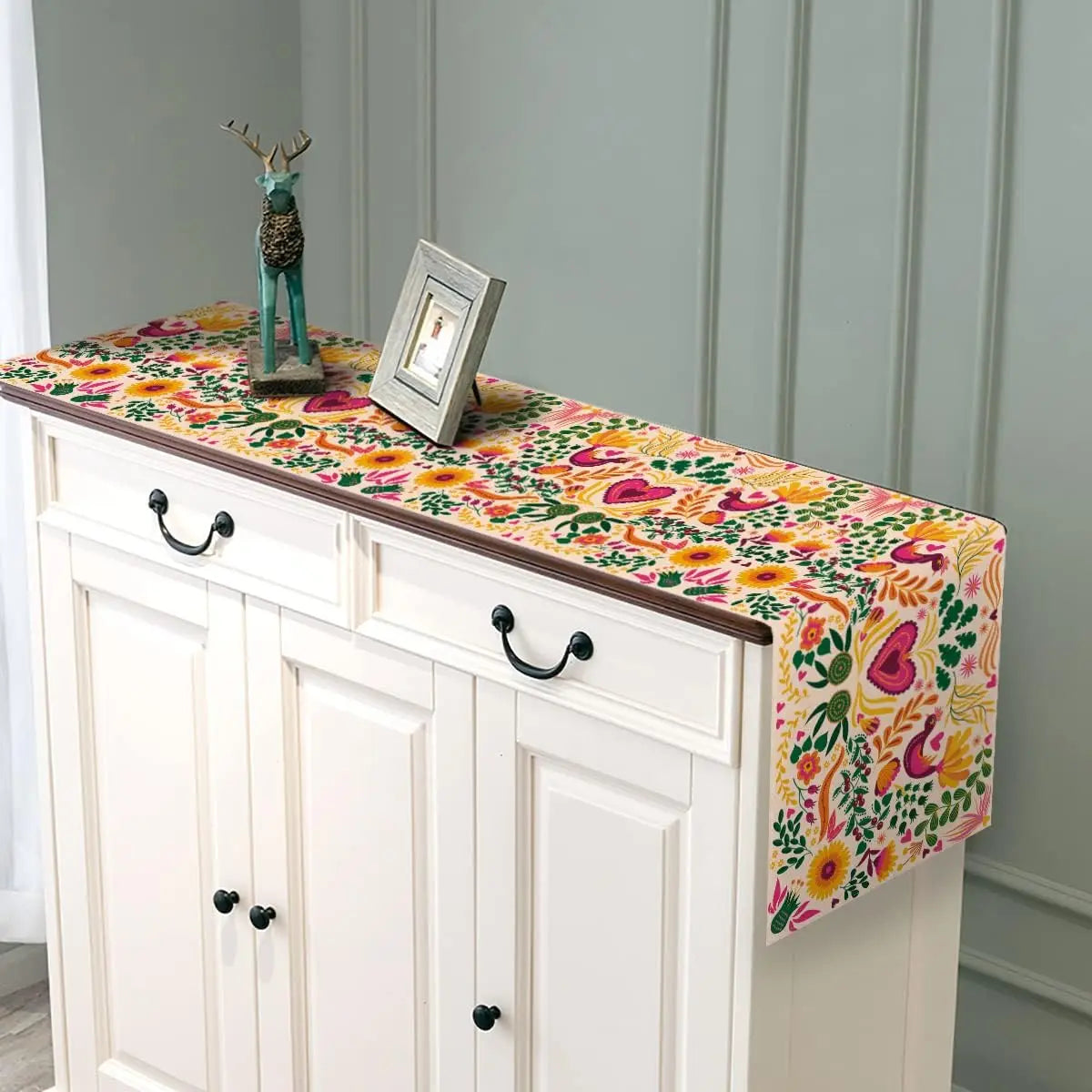 A white cabinet with a colorful Day of the Dead Mexican Fiesta table runner displayed on top.