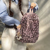 A person wearing a gray vest and blue shirt holds a pink leopard print nylon backpack.