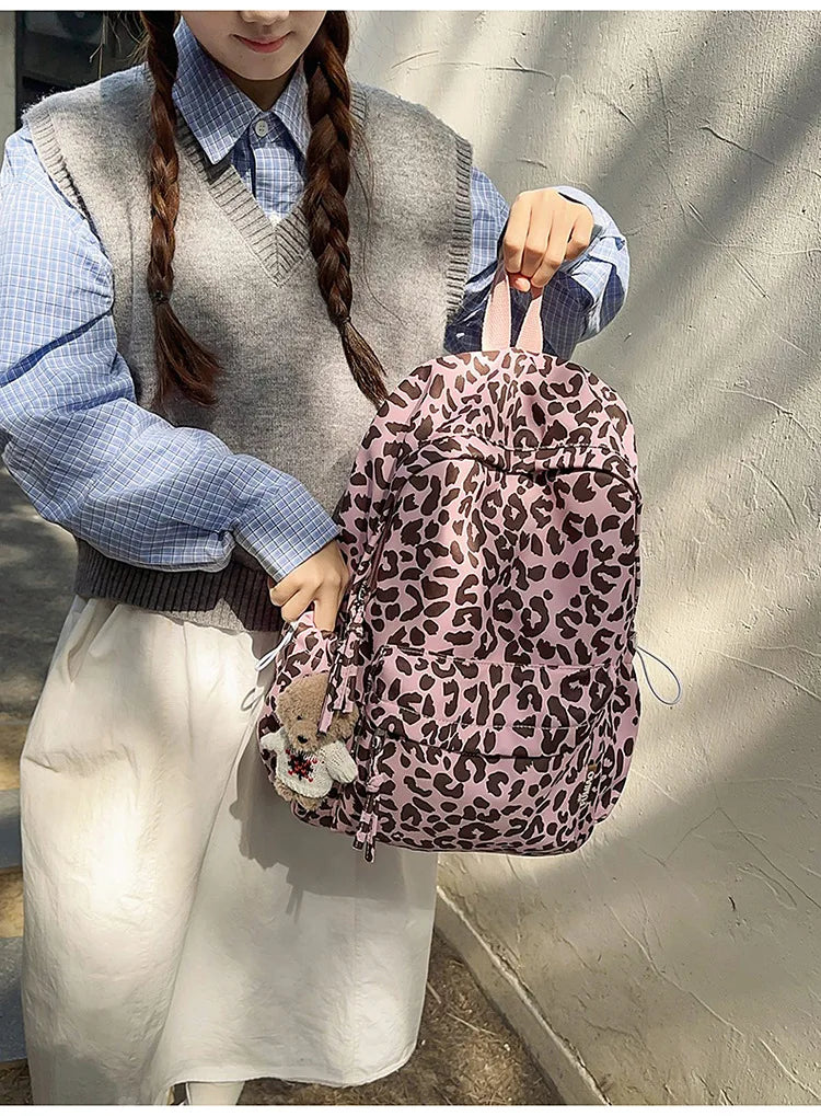 A person wearing a gray vest and blue shirt holds a pink leopard print nylon backpack.