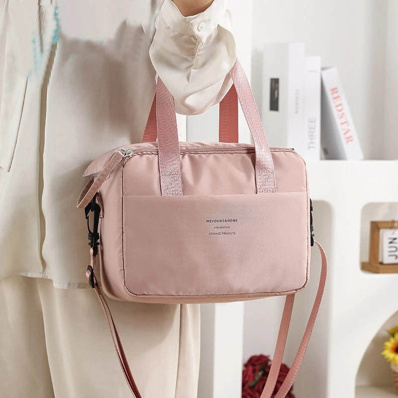 A pink compact thermal lunch tote bag is shown being held by a person, with white clothing and books in the background.