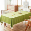 A lime green farmhouse tablecloth with white cotton tassels is displayed on a wooden dining table.