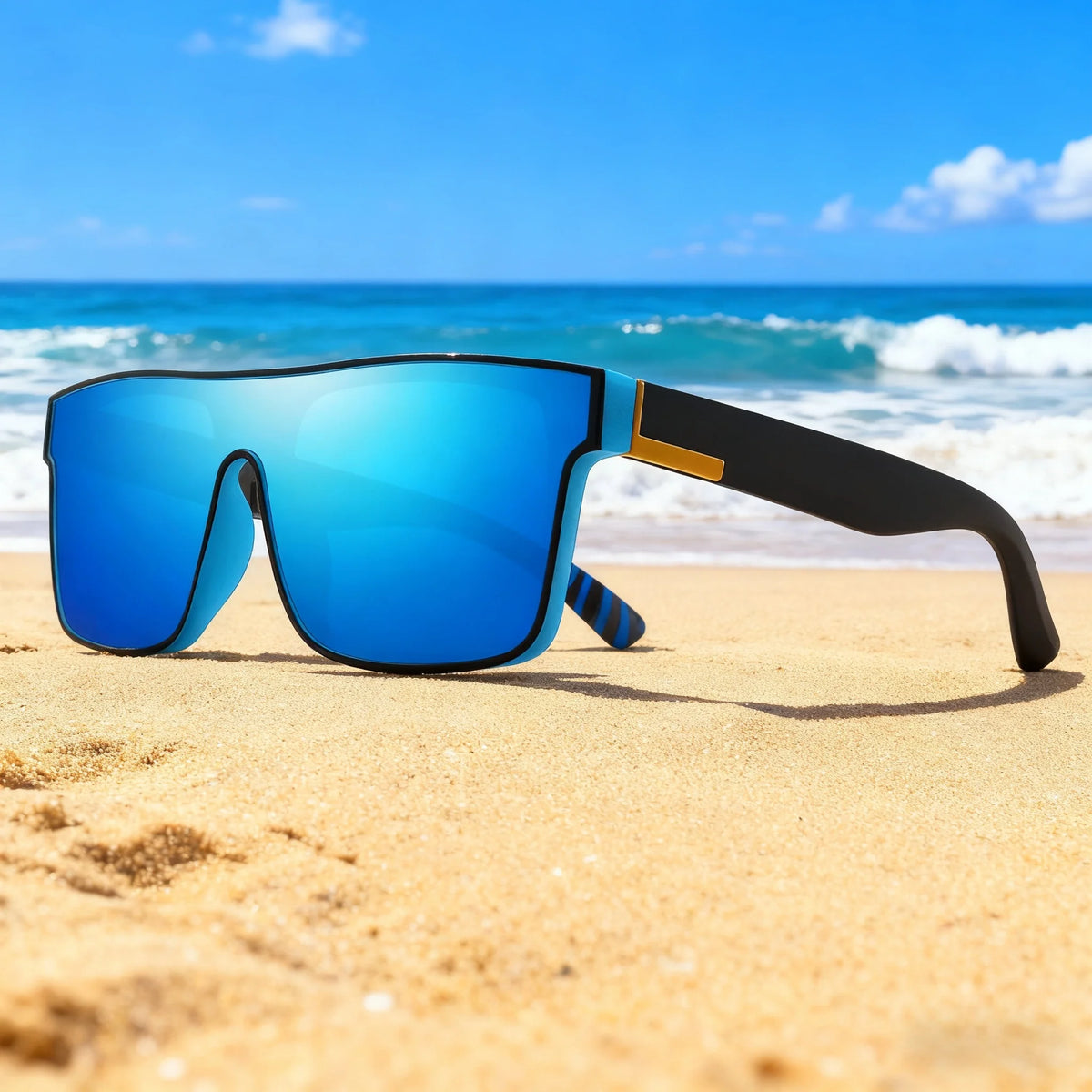 Blue sports sunglasses resting on golden sand with the ocean in the background.