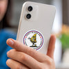 A hand holds a white smartphone displaying a funny meme sticker featuring a yellow pizza character.