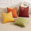 A collection of three ribbed corduroy throw pillows in orange, terracotta, and lime green resting on a beige surface.