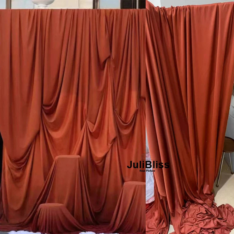 A close-up of rich burnt orange fabric draped in elegant folds for backdrops and decor.