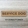 A brown woven patch with the text SERVICE DOG engraved on it, displayed on a light wooden surface.