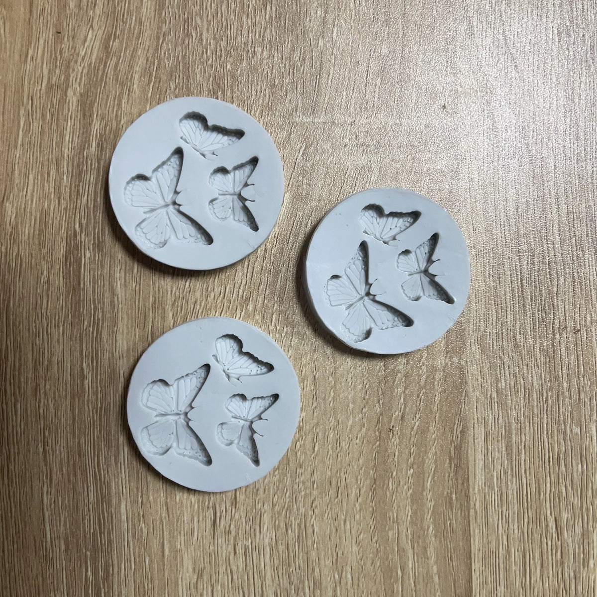 Four white silicone molds shaped like butterflies are arranged on a wooden surface.