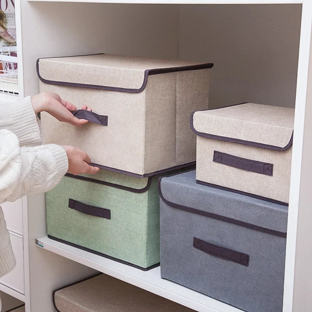 A hand is placing a beige fabric storage box onto a green and gray storage box set inside a white shelf.