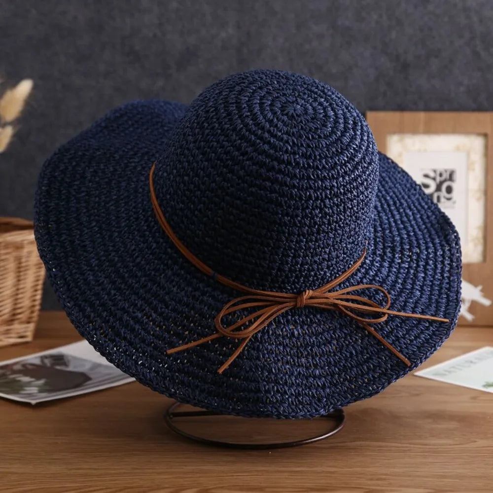 Sombrero de paja tejido azul marino oscuro con un cordón de cuero trenzado sobre una superficie de madera.