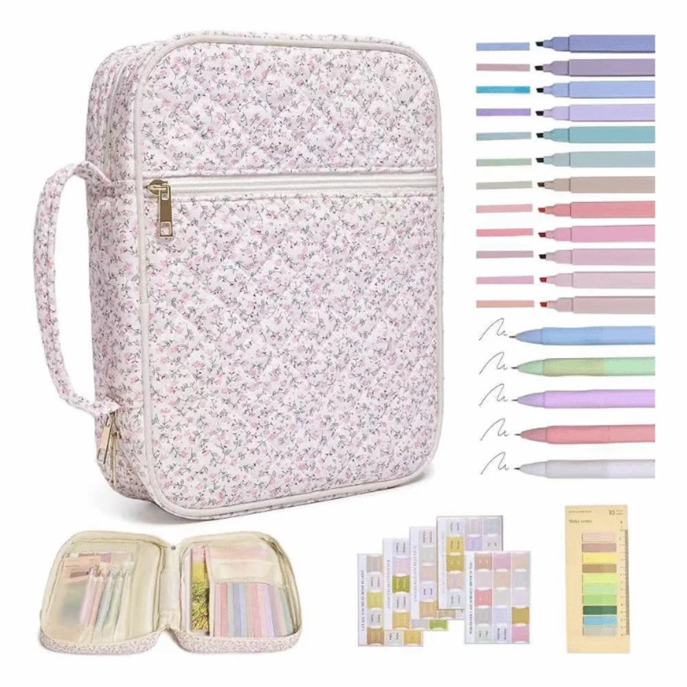 A floral quilted Bible cover with a zipper pocket and carry handle shown alongside various colored pens and pencils.