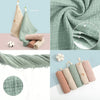 A collection of soft cotton gauze burp cloths in various shades of sage green and pink, including a folded cloth and a rolled