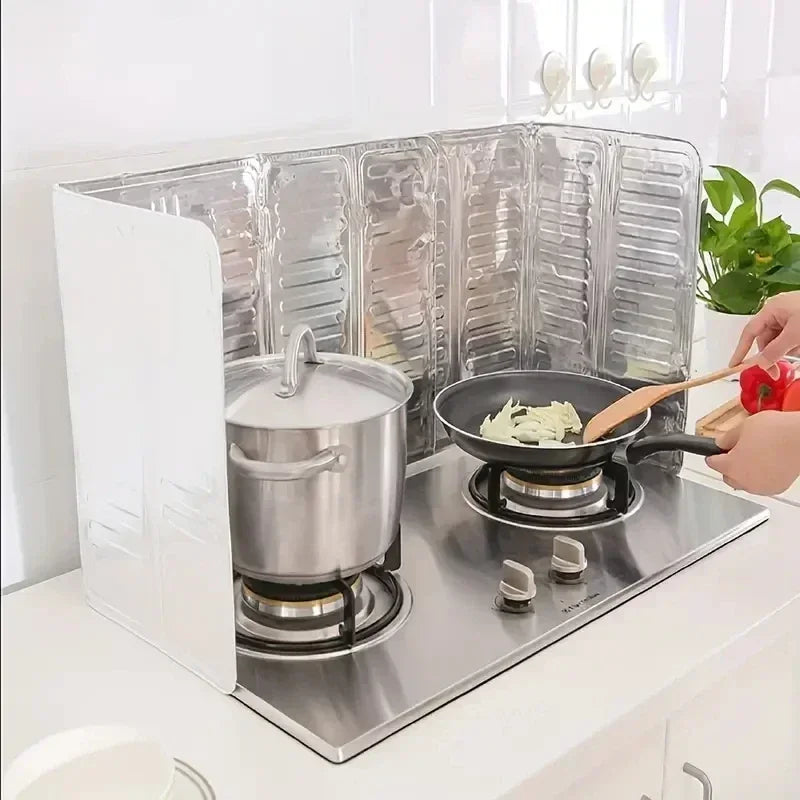 A foldable aluminum stove splatter guard is placed on a stovetop with a pot cooking on it.