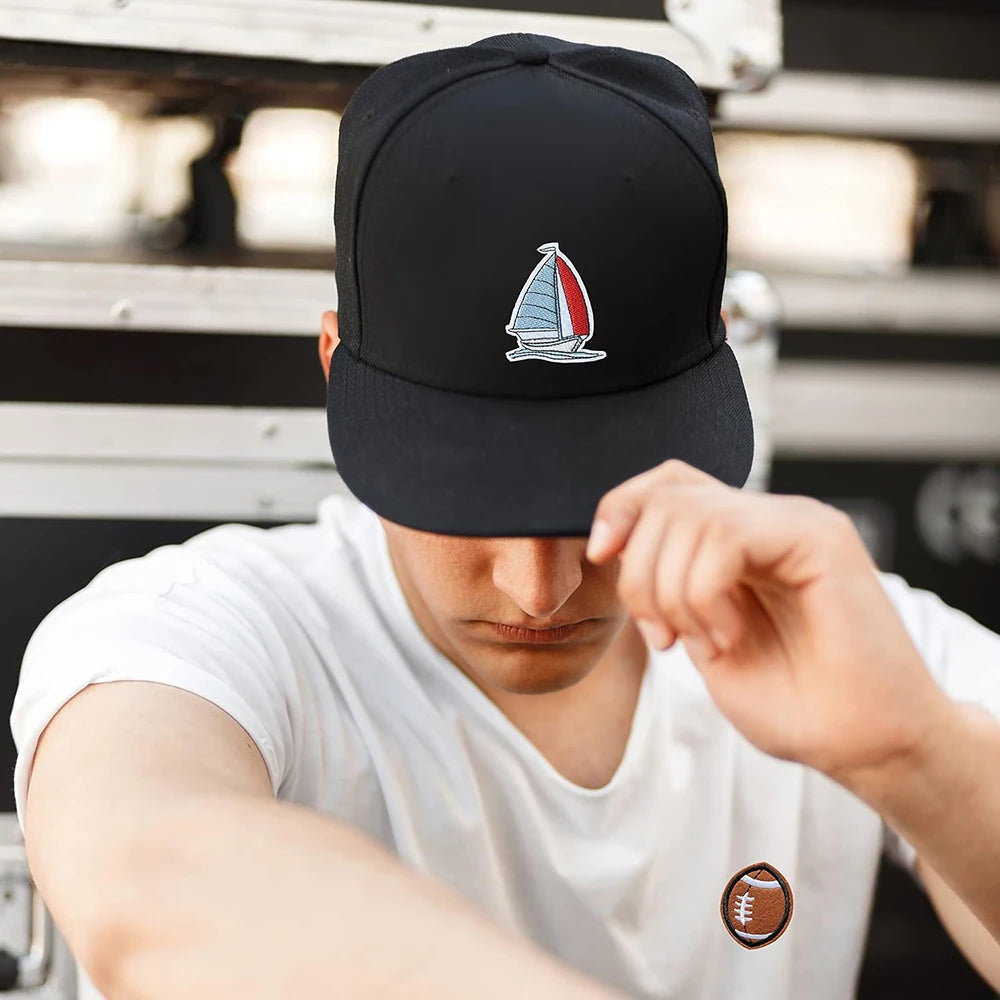 A close-up of a person wearing a black baseball cap with an embroidered sailboat patch on the front.