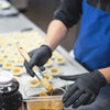 A person wearing black nitrile disposable gloves is using a paintbrush to apply a substance onto small yellow discs in a clea
