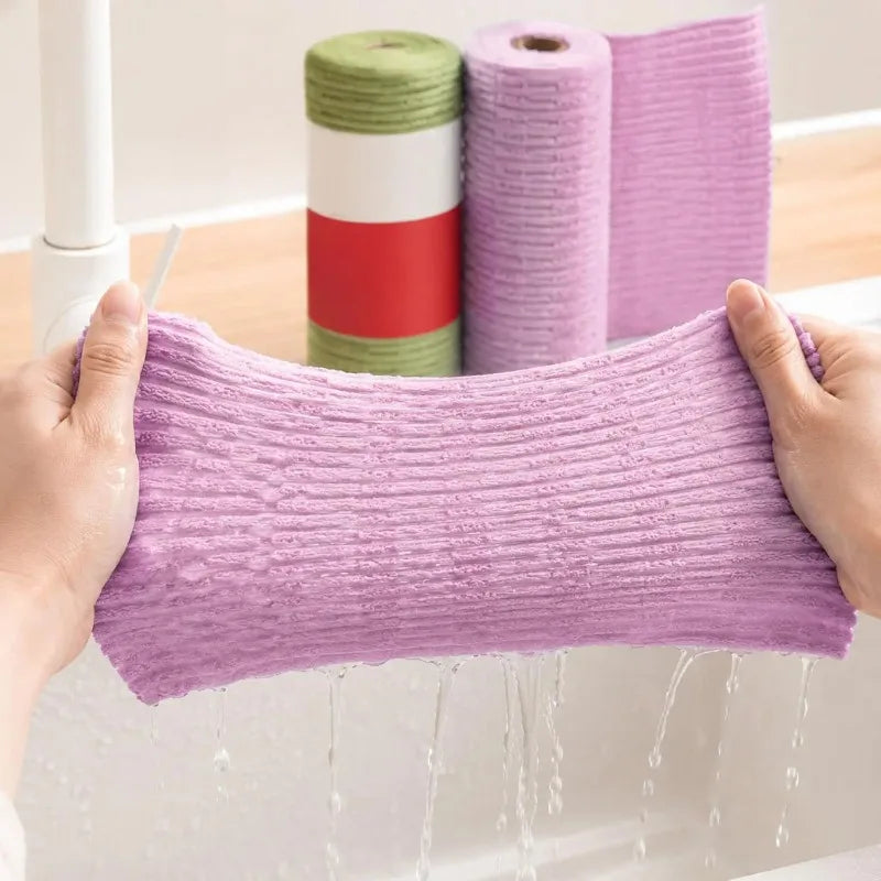 A hand is holding a purple reusable tear-away cleaning cloth, with rolls of similar cloths in green, red, and pink visible in