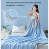 A woman is shown relaxing under a light blue cooling quilt on a bed, emphasizing natural coolness and refreshment.