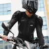 A person wearing a black motocross helmet and armor jacket is holding a dirt bike.