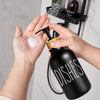 A hand is dispensing dish soap from a black bamboo pump dispenser onto a white sponge.